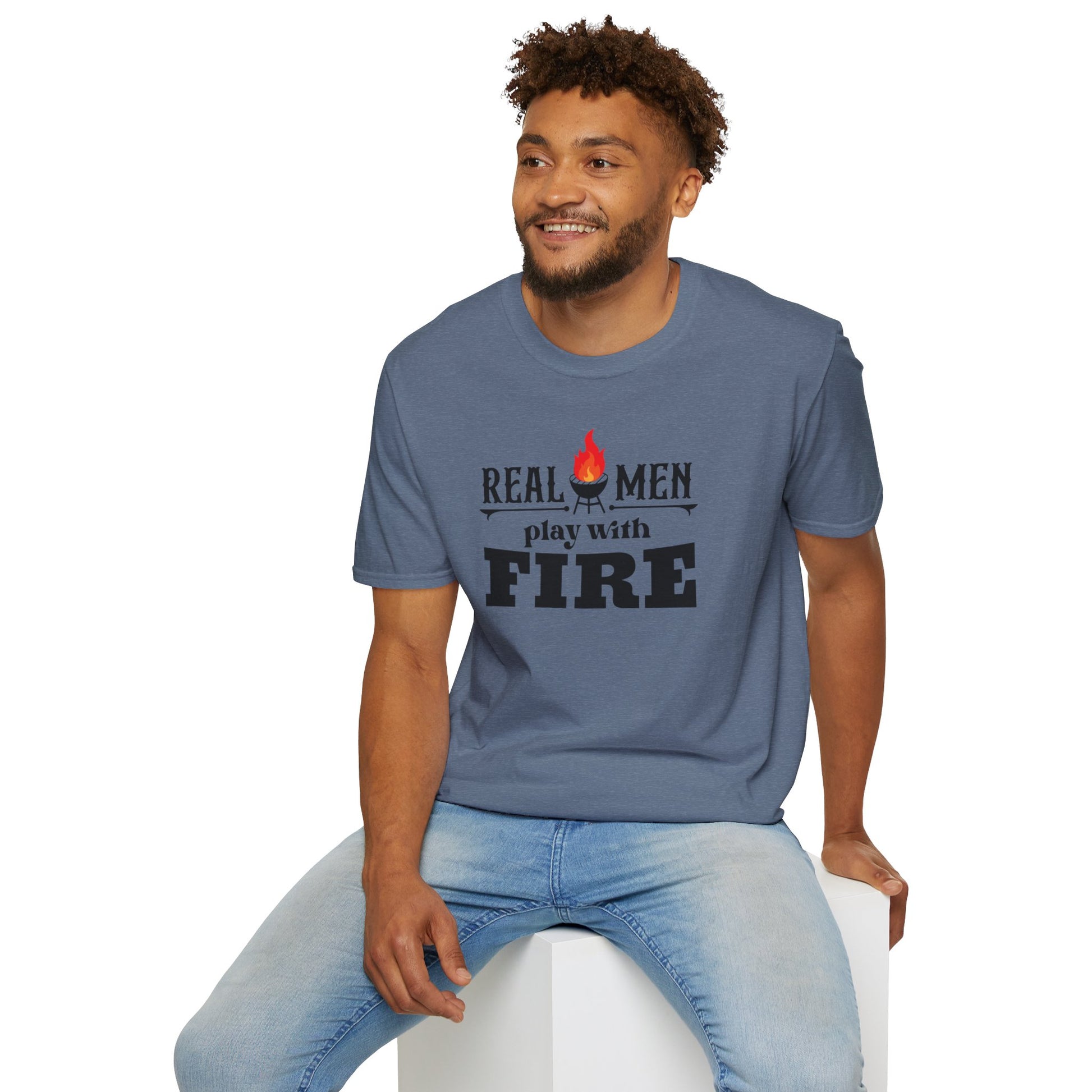 A gray-green Real Men Play With Fire - K.C. BBQ Inspired T-Shirt, featuring bold black letters and a flame icon above the "i" in "fire," is made from breathable lightweight fabric. Perfect for a casual ensemble, this shirt by KC Inspirations is displayed on a plain white background.