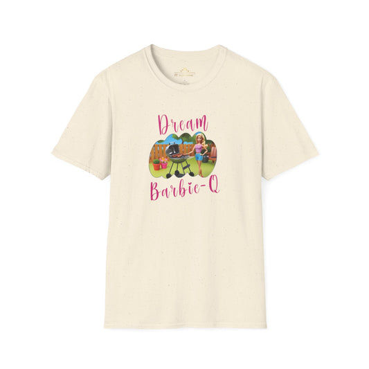 A beige T-shirt with speckles featuring a crisp graphic design of two dolls barbecuing in a backyard. The text "Dream Barbie-Q" is written in pink cursive above and below the image, making this Dream Barbie Q - K.C. BBQ Inspired T-Shirt by KC Inspirations perfect for fans of Kansas City BBQ.