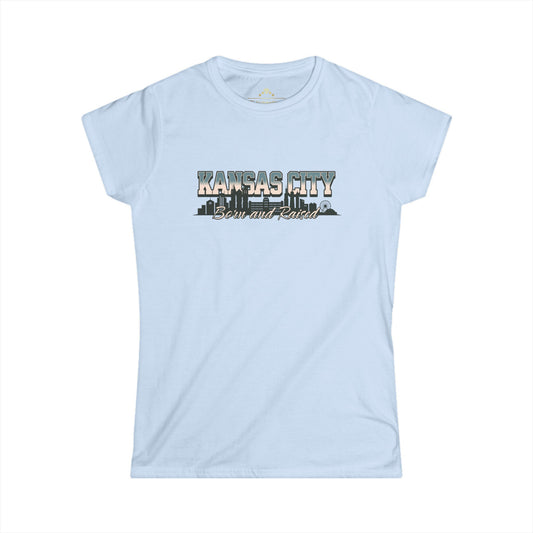 Light blue Born And Raised KC - Kansas City Inspired Women's T-Shirt by KC Inspirations with "KANSAS CITY Born and Raised" written on the front. The text features a city skyline silhouette integrated within the lettering, perfect for showing off your hometown pride.