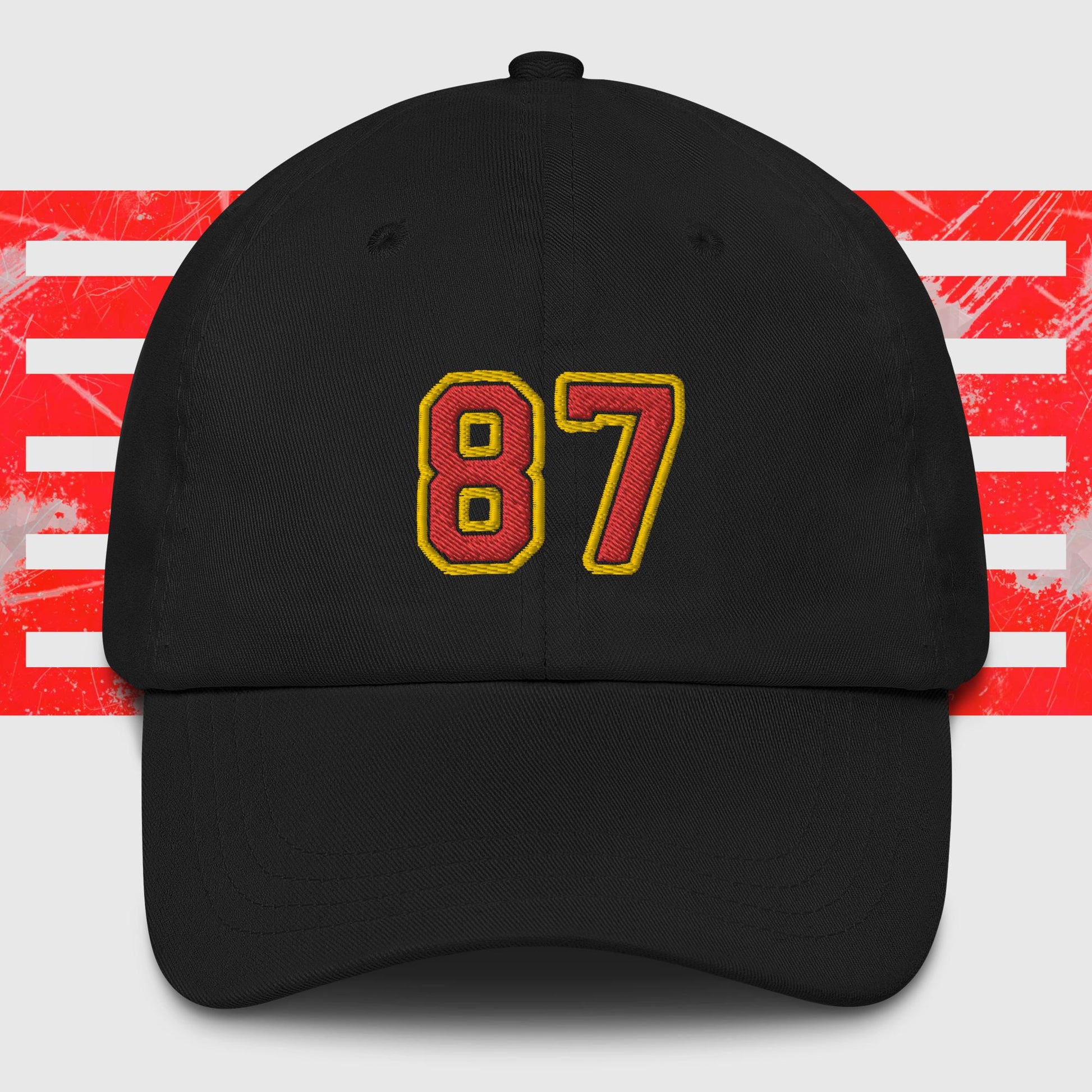 A Red & Gold 87 - Kansas City Chiefs Inspired Cap by KC Inspirations with the number "87" embroidered on the front in bold yellow and red colors. In the background, there is a pattern featuring red horizontal stripes over a white backdrop, reminiscent of Kansas City Chiefs' vibrant spirit.