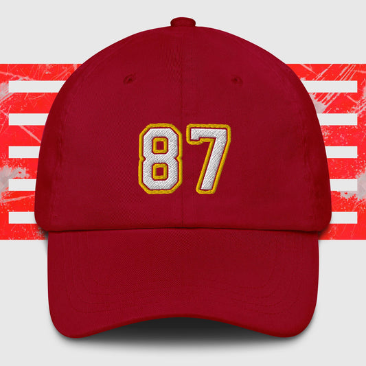 A White & Gold 87 - Kansas City Chiefs Inspired Cap from KC Inspirations. The background features red and white horizontal stripes with a distressed texture, reminiscent of Kansas City Chiefs spirit.