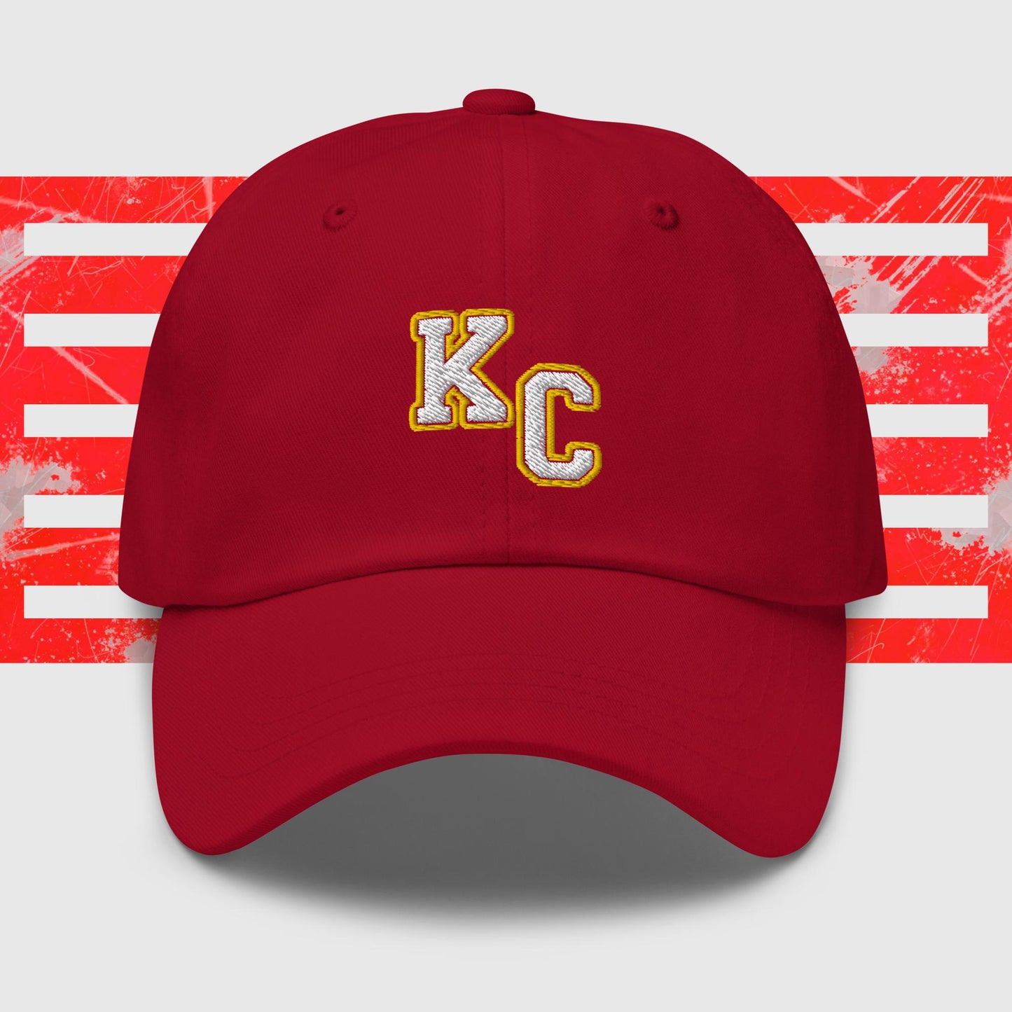 Red KC Inspirations Kansas City Chiefs Inspired Cap with gold letters "KC" embroidered on the front. The background features a stylized American flag with red stripes and white stars, appearing distressed or splattered with paint. This KC White & Gold - Kansas City Chiefs Inspired Cap comes with an adjustable strap and has a curved brim.