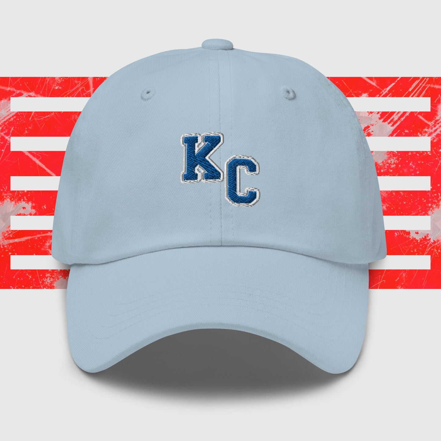 A Blue KC - Kansas City Royals Inspired Cap from KC Inspirations featuring the white block letters "K" and "C" outlined in dark blue on the front. The background includes horizontal red and white stripes with a distressed texture, accentuated by embroidered graphics, making it the perfect dad hat for any fan.