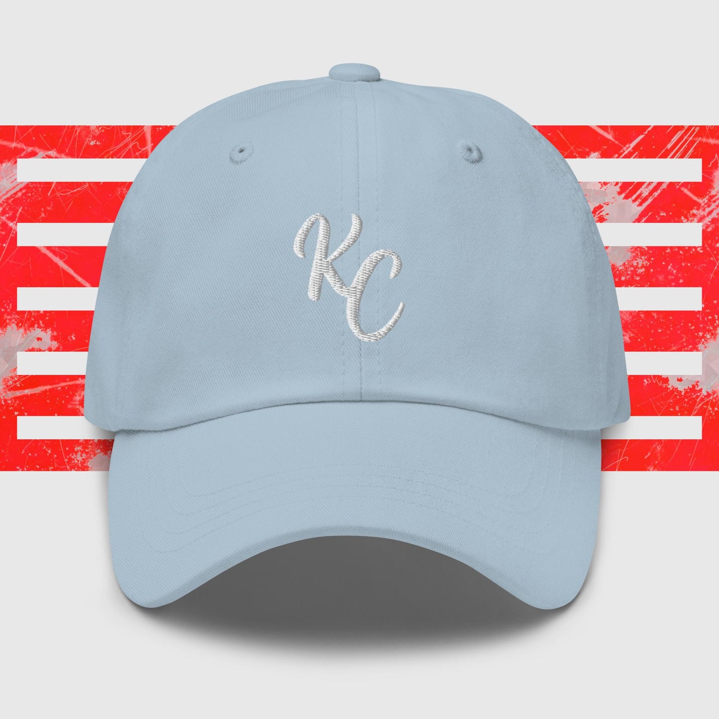 A **light blue Kansas City Royals cap** with an embroidered white "KC" logo on the front, displayed against a background featuring horizontal red and white distressed stripes.

Replace with:

A **White KC - Kansas City Royals Inspired Cap by KC Inspirations** with an embroidered white "KC" logo on the front, displayed against a background featuring horizontal red and white distressed stripes.