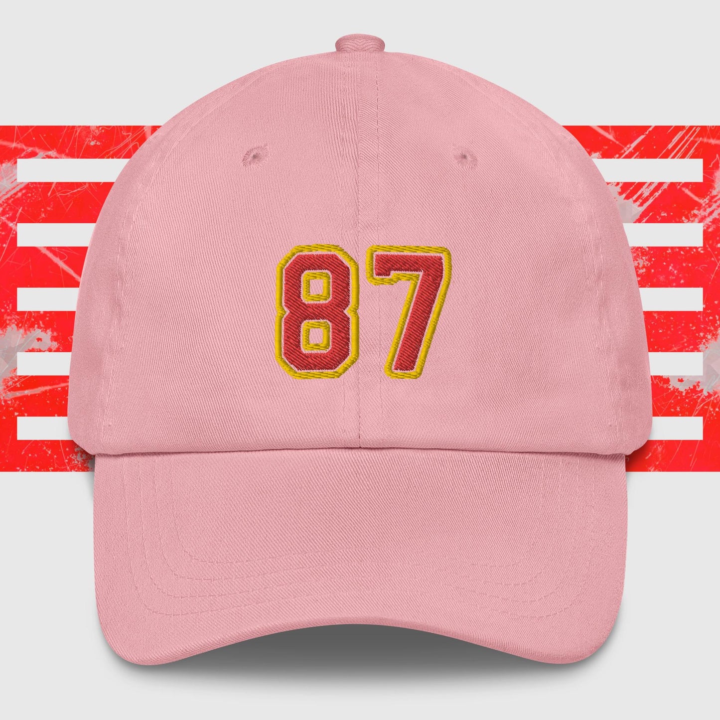 A Red & Gold 87 - Kansas City Chiefs Inspired Cap by KC Inspirations with the number "87" embroidered on the front in bold yellow and red colors. In the background, there is a pattern featuring red horizontal stripes over a white backdrop, reminiscent of Kansas City Chiefs' vibrant spirit.