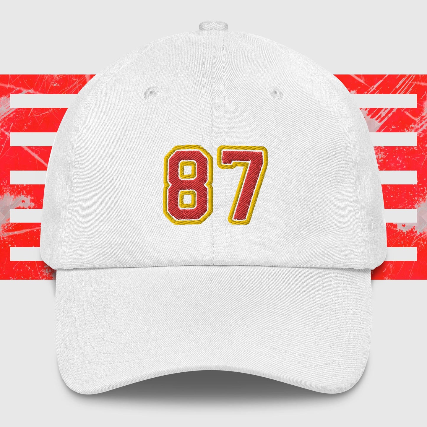 A Red & Gold 87 - Kansas City Chiefs Inspired Cap by KC Inspirations with the number "87" embroidered on the front in bold yellow and red colors. In the background, there is a pattern featuring red horizontal stripes over a white backdrop, reminiscent of Kansas City Chiefs' vibrant spirit.